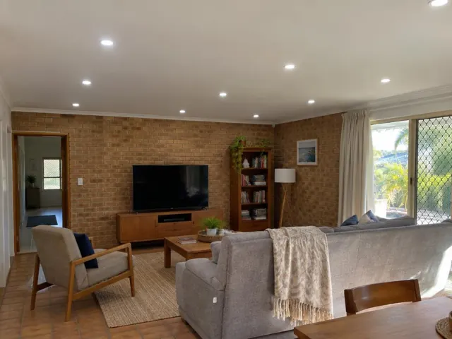 Living room with recessed ceiling downlights, brick walls, sofa and TV in a home in Elanora